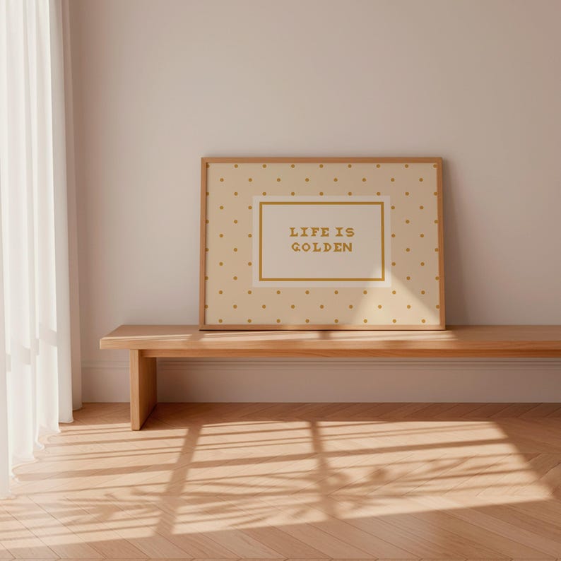 Puede incluir: Una pieza de arte mural rectangular enmarcada con un fondo crema claro y un patr&oacute;n repetitivo de peque&ntilde;os puntos dorados. Centrado dentro de un borde rectangular dorado se encuentra el texto "LIFE IS GOLDEN" en una fuente sans-serif dorada.