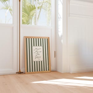 Może przedstawiać: Oprawiony wydruk artystyczny ze złotą ramą. Grafika przedstawia zielono-białe paski z tekstem "Meet Me On The Green" pośrodku. Wydruk opiera się o białą ścianę i drewnianą podłogę.
