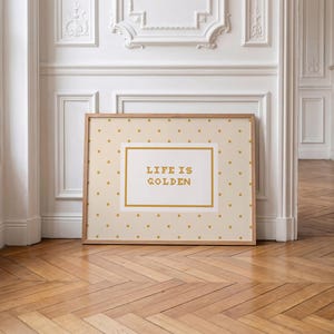 Puede incluir: Una impresi&oacute;n rectangular enmarcada con un fondo beige claro y un patr&oacute;n repetitivo de peque&ntilde;os puntos dorados. En el centro, un panel rectangular blanco con borde dorado muestra el texto "LIFE IS GOLDEN" en letras doradas en negrita.