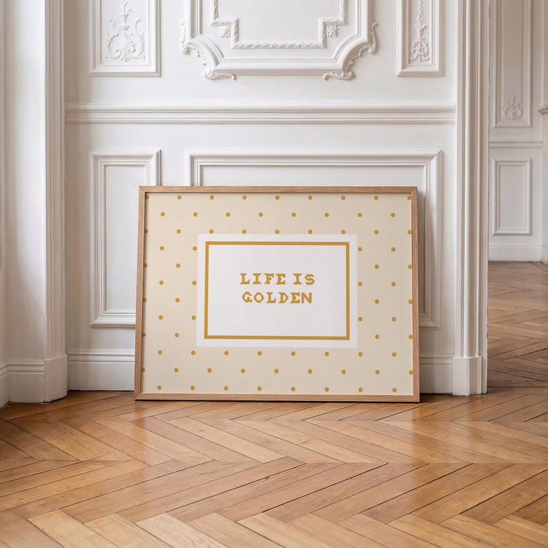 Puede incluir: Una impresi&oacute;n rectangular enmarcada con un fondo beige claro y un patr&oacute;n repetitivo de peque&ntilde;os puntos dorados. En el centro, un panel rectangular blanco con borde dorado muestra el texto "LIFE IS GOLDEN" en letras doradas en negrita.