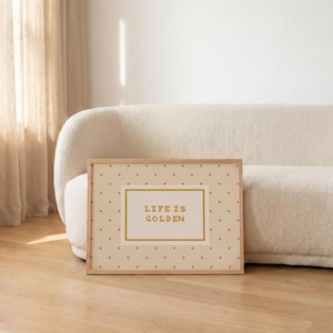 Puede incluir: Una impresi&oacute;n rectangular enmarcada con un fondo crema claro y un patr&oacute;n repetitivo de peque&ntilde;os puntos dorados. En el centro, un recuadro rectangular con borde dorado contiene el texto "LIFE IS GOLDEN" impreso en una fuente dorada en negrita.