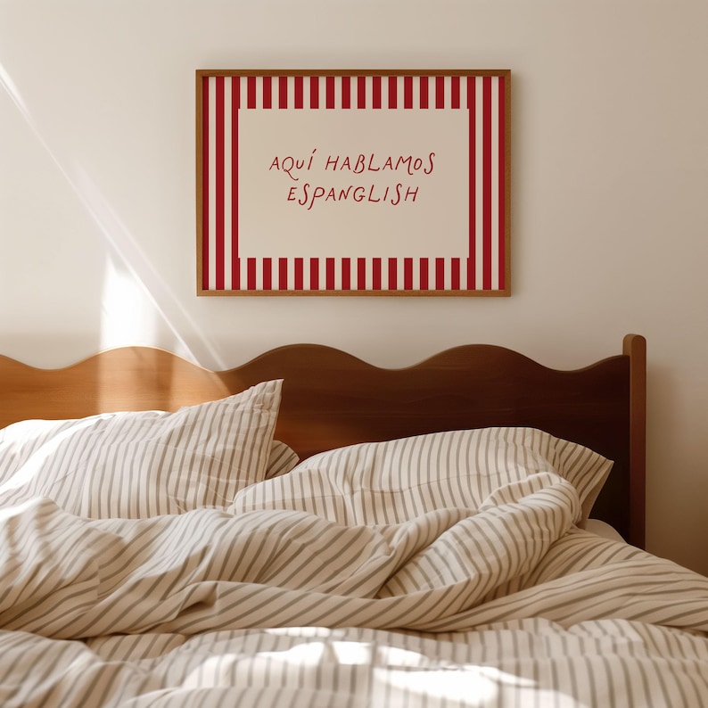 May include: A rectangular wall art print in a wooden frame featuring a red and white vertical striped border surrounding a cream-coloured centre. The text "AQU&Iacute; HABLAMOS ESPANGLISH" is printed in red, handwritten-style lettering in the middle.