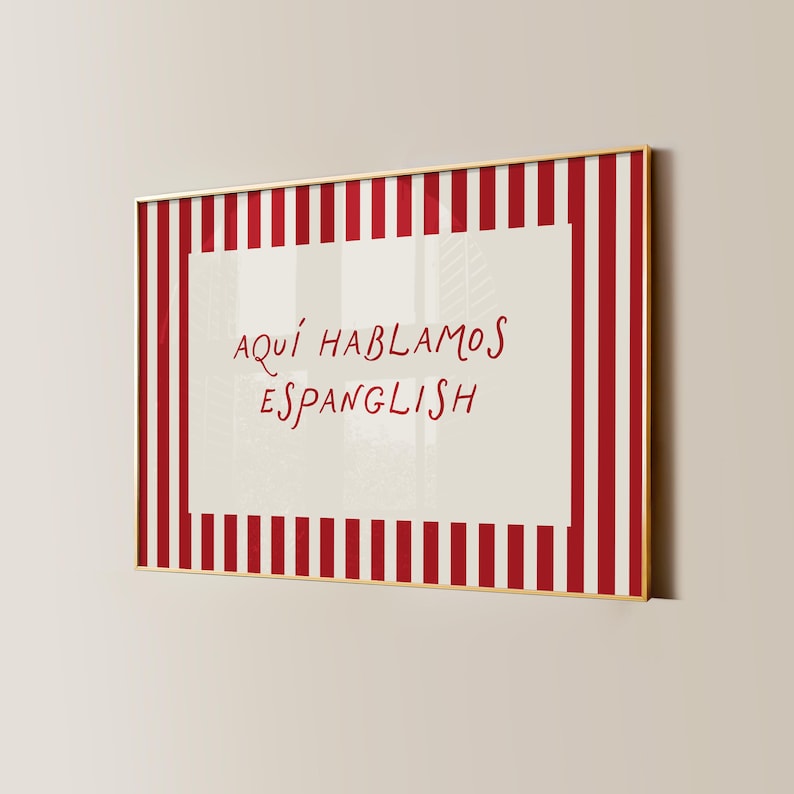 May include: A rectangular framed wall art piece featuring a cream-coloured centre with the red handwritten text 'AQU&Iacute; HABLAMOS ESPANGLISH'. The border consists of vertical red and white stripes, all enclosed within a thin gold-coloured metal frame.