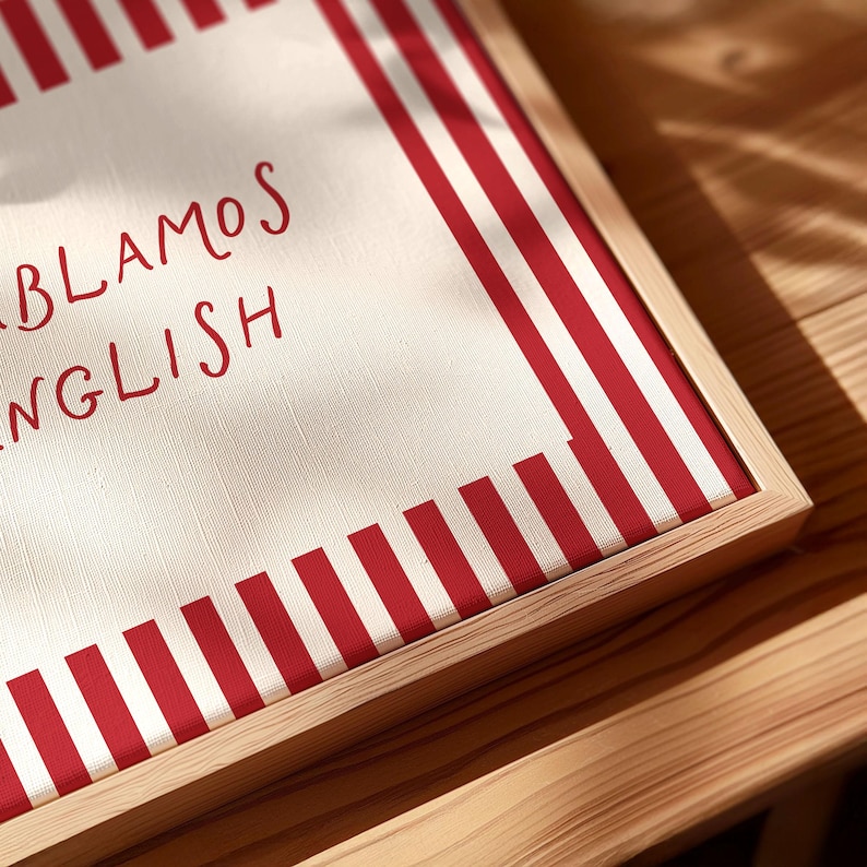 May include: A square canvas print in a light wood frame featuring a white background with vertical red stripes along the edges. The text "HABLAMOS ENGLISH" is printed in red, handwritten-style lettering on the left side of the canvas surface.