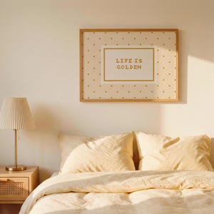 Puede incluir: Una l&aacute;mina decorativa rectangular en un marco de madera clara con fondo crema y un patr&oacute;n de peque&ntilde;os puntos dorados. En el centro, un recuadro blanco con borde dorado contiene el texto "LIFE IS GOLDEN" en letras doradas.