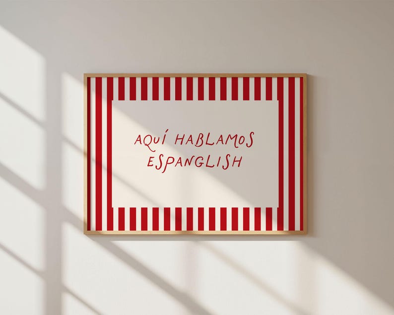 May include: A rectangular wall art print in a light wood frame featuring a white centre panel with the red text 'AQU&Iacute; HABLAMOS ESPANGLISH'. The border consists of vertical red and white stripes surrounding the central text area.