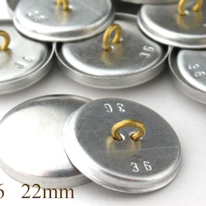 May include: A close-up of a pile of silver metal buttons with a brass loop on the top. The buttons are marked with the number 36 and are 22mm in diameter.