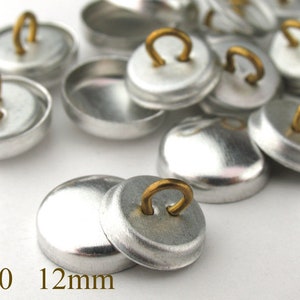 Op de afbeelding: Een close-up van zilveren metalen knopen met een gouden lus aan de bovenkant. De knopen zijn 12 mm in diameter en zijn gemarkeerd met #20.