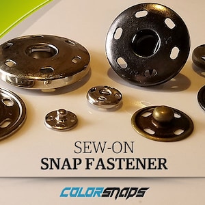 May include: A set of sew-on snap fasteners in various finishes, including silver, black, and brass. The snaps are designed for use in clothing and other fabric projects.  The text "SEW-ON SNAP FASTENER" is printed below the snaps. The text "COLORSNAPS" is printed below the text.