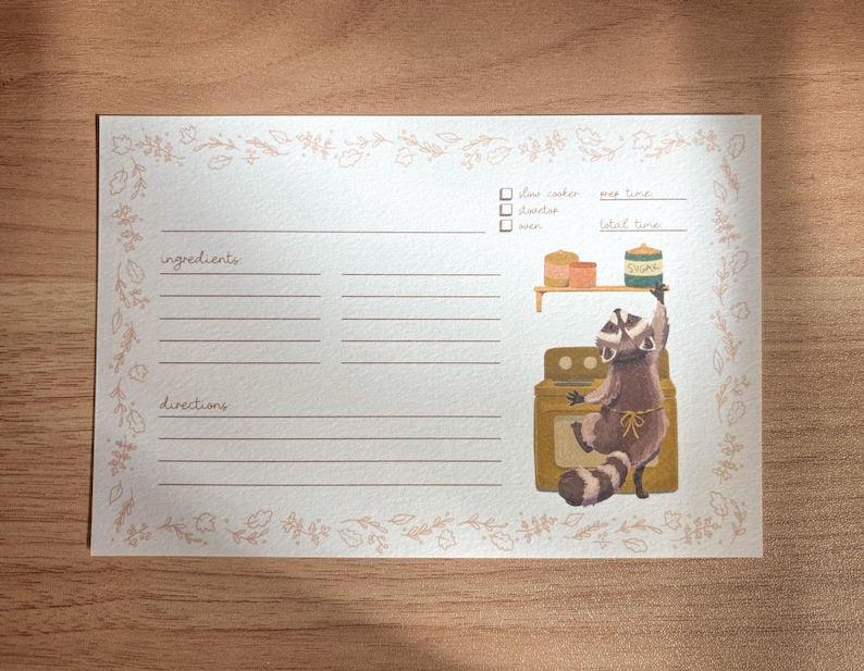May include: A printable recipe card with a raccoon illustration. The card has a floral border and sections for ingredients and directions. The raccoon is wearing a chef's hat and holding a jar of jam. The text on the card reads "flour, sugar, oven, prep time, total time".