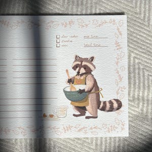 May include: A printable recipe card featuring a raccoon wearing an apron and holding a wooden spoon. The card has a floral border and lines for writing down ingredients and instructions. The text on the card reads "slow cooker", "wet time", "total time", and "other".