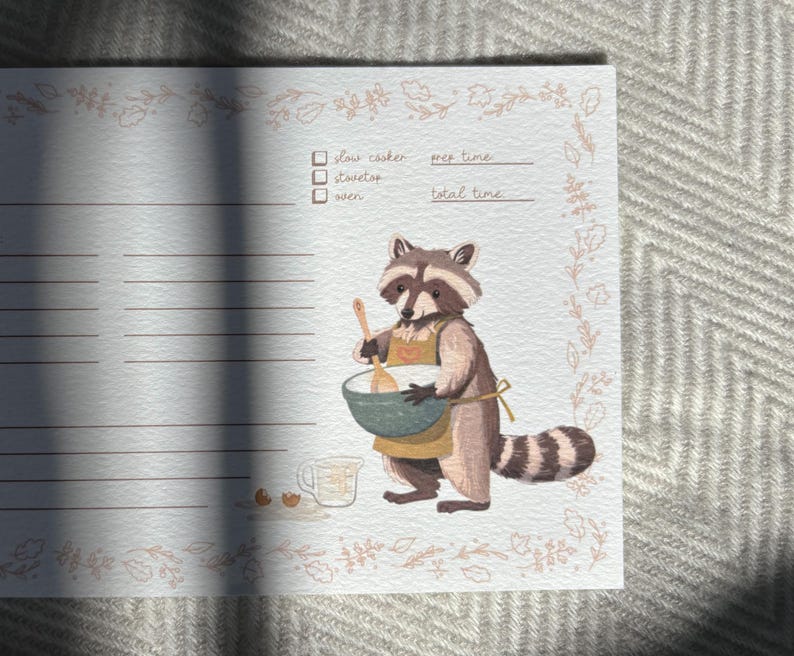 May include: A printable recipe card featuring a raccoon wearing an apron and holding a wooden spoon. The card has a floral border and lines for writing down ingredients and instructions. The text on the card reads "slow cooker", "wet time", "total time", and "other".