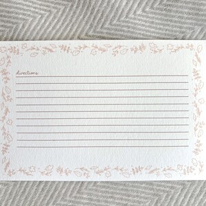 May include: A blank recipe card with a floral border in a light pink color. The card has lines for writing directions and the word "directions" is written at the top.