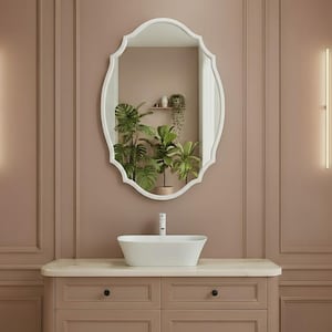 Pode incluir: Uma bancada de casa de banho com um espelho oval branco, uma pia de vaso branca e um armário em cor rosa suave. O espelho reflete plantas. Duas luzes verticais estão na parede. A bancada tem ferragens pretas.