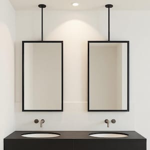 Pode incluir: Uma moderna casa de banho com dois espelhos retangulares suspensos do teto. Os espelhos têm molduras pretas. Abaixo, uma bancada preta flutuante com duas pias ovais e torneiras de bronze. As paredes são brancas com azulejos brancos.