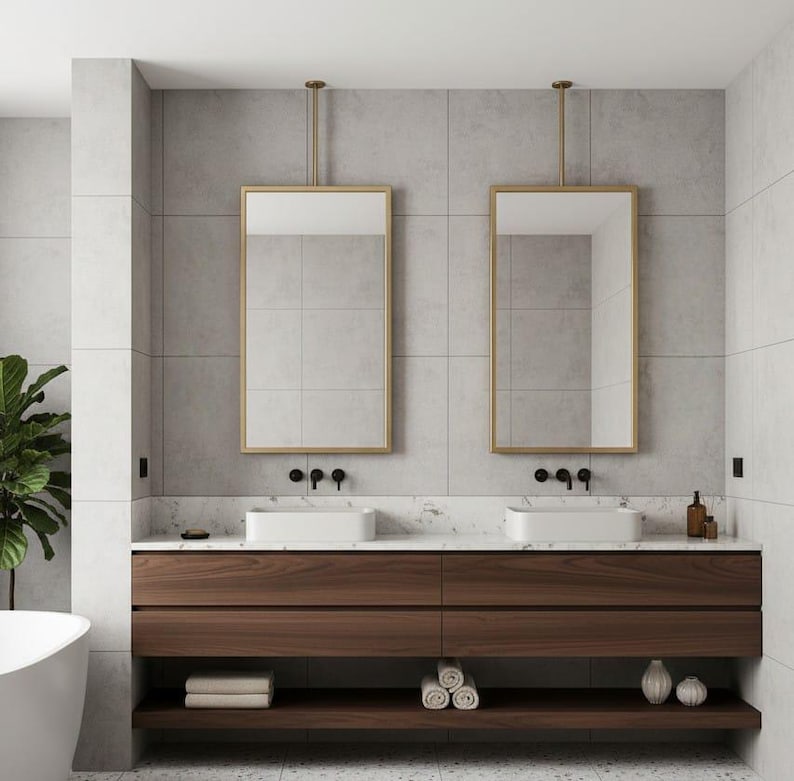 May include: A double bathroom vanity featuring a dark wood cabinet with two open shelves, topped with a white marble counter, two rectangular white vessel sinks, two gold-framed hanging mirrors, and matte black wall-mounted faucets.