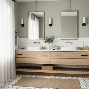 May include: A double bathroom vanity with light wood cabinets, two white rectangular vessel sinks, and two gold-framed mirrors suspended from the ceiling. The wall features white subway tiles and sage green paint, with a slatted wood shelf below.