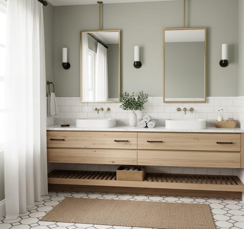 May include: A double bathroom vanity with light wood cabinets, two white rectangular vessel sinks, and two gold-framed mirrors suspended from the ceiling. The wall features white subway tiles and sage green paint, with a slatted wood shelf below.