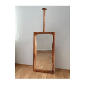 Pode incluir: Um espelho com moldura de madeira com um design curvo único. O espelho está pendurado em uma haste de madeira presa ao topo da moldura.