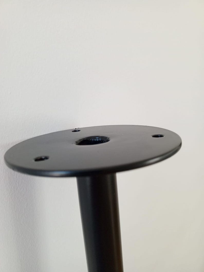 Może przedstawiać: Czarna metalowa noga stołu z okrągłą podstawą i trzema otworami na śruby. Podstawa ma średnicę około 10 cm.