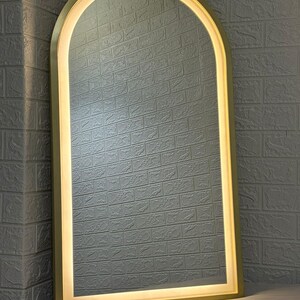 May include: An arched floor mirror featuring a metallic gold frame and an integrated LED light strip that follows the curved top and straight sides, providing a bright, even glow around the reflective glass surface of the tall mirror.