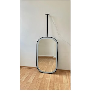 May include: A black framed oval mirror with a white border hangs from the ceiling. The mirror is reflecting a wooden floor.