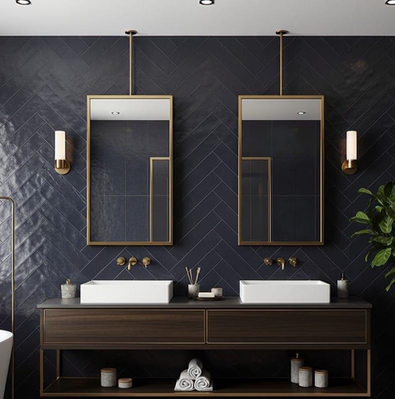 May include: A double vanity bathroom setup featuring two rectangular white vessel sinks on a dark wood cabinet with a lower shelf. Two rectangular mirrors with gold frames hang from the ceiling above the sinks, flanked by two wall-mounted lights.