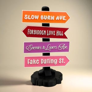 Könnte beinhalten: Ein schwarzer Wegweiser mit vier Richtungsschildern. Die Schilder sind orange, rot, lila und rosa, jedes mit weißem Text: "SLOW BURN AVE.", "FORBIDDEN LOVE HILL", "Enemies to Lovers Ave.", und "Fake Dating St."