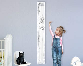 May include: White wooden growth chart with a distressed wood finish. The chart features a ruler with measurements in inches and feet. The text "loved beyond measure" is at the top of the chart. The name "Charlotte" is written in cursive on the right side of the chart. A young girl is standing next to the chart, measuring her height.