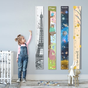 May include: Four colorful personalized growth charts with different themes. The charts feature a black and white Eiffel Tower, a pink moose, a blue and black space theme, and a yellow and brown bee theme. Each chart has a name at the top and a measurement scale in inches.