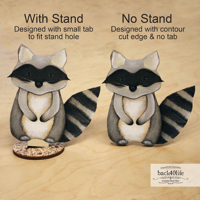 May include: Two papercraft raccoon figurines, one with a stand and one without. The raccoon with the stand has a small tab to fit into the stand hole. The raccoon without the stand has a contour cut edge. Both raccoons have black and white striped tails and are painted in shades of grey, brown, and white.