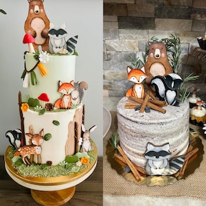 May include: Two tiered cakes decorated with woodland animal figurines. The bottom tier is a white cake with brown tree bark and green leaves. The top tier is a green cake with a brown bear, raccoon, fox, and squirrel figurines. The cakes are on a gold stand.