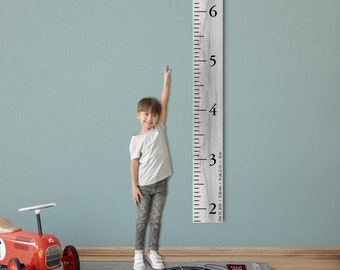 Op de afbeelding: Een witte houten groeimeter met zwarte markeringen en de naam "Lucas" bovenaan. Een kind staat naast de meter en reikt tot de 122 cm-markering.