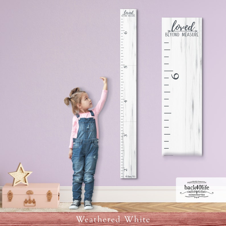 May include: A weathered white wooden growth chart with a white and gray woodgrain pattern. The chart features a ruler with markings from 2 to 6 feet. The text "loved beyond measure" is printed in black at the top of the chart. The chart is mounted on a light purple wall.