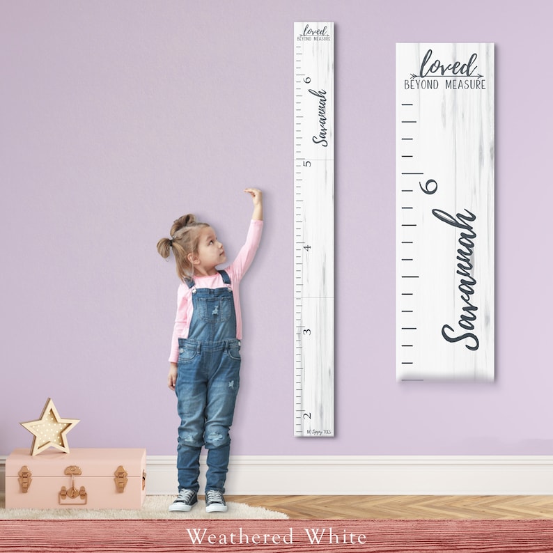 May include: A white wooden growth chart with a weathered finish. The chart features a black and white woodgrain pattern and the text "loved beyond measure" and "Savannah".