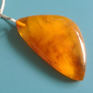 May include: A pendant necklace featuring a large, teardrop-shaped amber stone. The amber is a warm, honey colour with visible inclusions. The pendant is attached to a silver chain.