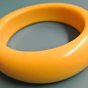 Op de afbeelding: Een gladde, lichtgele plastic armband. De armband is dik en heeft een afgeronde vorm.