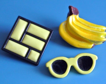 Lot of 3 vintage 1950s unused small lucite plastic yellow/ black or brown brooches with banana/sunglass/abstract motive and securety needle
