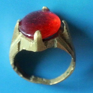 May include: A gold ring with a large, red, glass gemstone set in the center.
