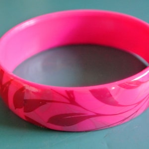 Könnte beinhalten: Ein pinkfarbenes Plastikarmband mit einem floralen Design in einem dunkleren Rosaton.