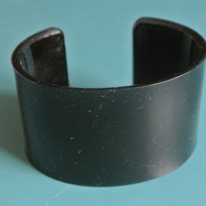 Könnte beinhalten: Ein schwarzes Plastikarmband mit glatter, matter Oberfläche.