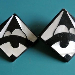 Op de afbeelding: Een paar geometrische oorbellen in zwart en wit met een driehoekige vorm. De oorbellen hebben een wit centrum met een zwarte omtrek.