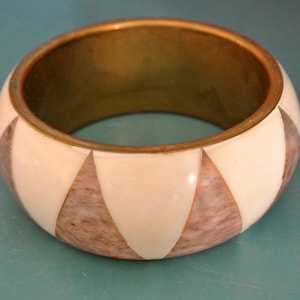 May include: A white and brown patterned bangle bracelet with a gold metal band.