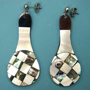 May include: A pair of drop earrings with a distinctive design. The earrings have a black top, a white and iridescent shell middle section, and a checkered pattern at the bottom. They have silver-coloured ear wires.