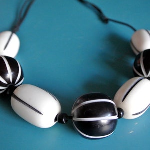 Op de afbeelding: Een zwart-witte kralenketting met afwisselend ronde en ovale kralen. De kralen hebben een gestreept patroon.