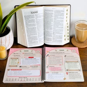 May include: An open Bible with the book of Isaiah displayed, alongside a study guide with pink accents. A cup of coffee and a lit candle are also visible. The Bible is open to chapter 1.
