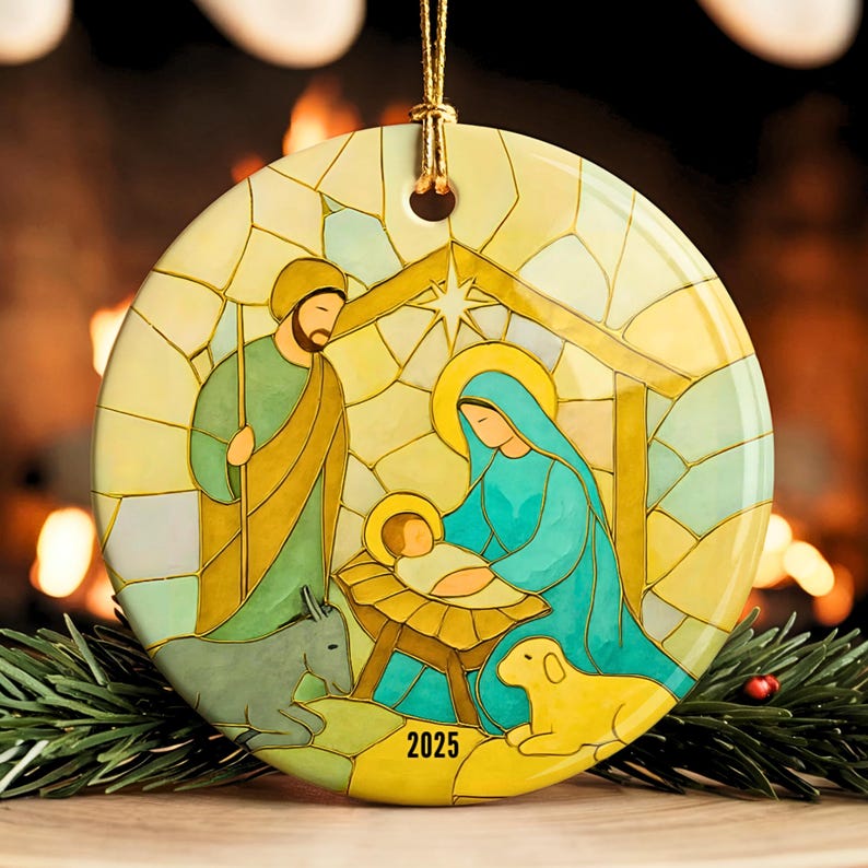 May include: Round Christmas ornament featuring a stained-glass style depiction of the Nativity scene. The ornament shows Mary, Joseph, and baby Jesus, with a donkey and a lamb. The year "2025" is printed on the bottom.