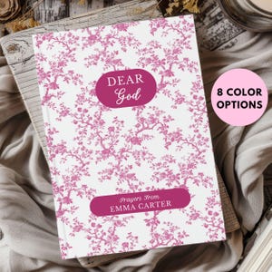 May include: A white journal with a pink floral pattern and the text "DEAR God" in a pink circle. The text "Prayers From EMMA CARTER" is in a pink rectangle at the bottom of the journal.