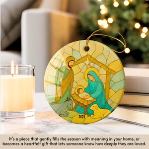 May include: A round Christmas ornament featuring a Nativity scene with Mary, Joseph, and baby Jesus. The ornament has a gold string for hanging and the year 2025 is printed on the bottom. The artwork is in shades of green, blue, and yellow.