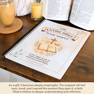 May include: A spiral-bound book titled "The Entire Bible Made Simple" with a floral and religious design. The cover features an open Bible, a cross, and a crown. The book is on a wooden surface, with a glass of coffee and a candle in the background.